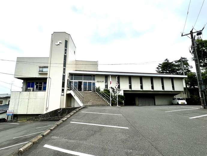 ゆるやかな坂道と駐車スペースの奥に、白く近代的なデザインの庁舎がそびえ立ち、建物の中央にある階段を上った先に入口が見える須賀川商工会議所の写真