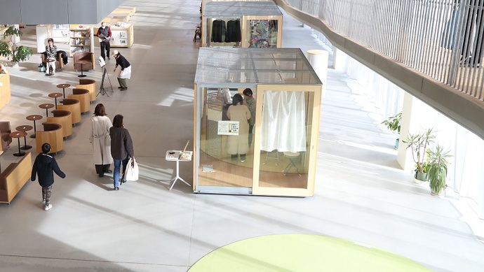 広々としたモダンな建物の須賀川市民交流センターtette内で左側にはソファとテーブルが並んだスペース、中央にはガラス張りのブースが2つ設置され商品などが陳列されているチャレンジショップを見下ろすように撮影した写真