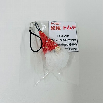 透明な袋に入った「妖精 トムテ」の説明書きと共に、星柄の赤い帽子を被り白い髭を蓄えた北欧の妖精トムテのストラップが収められており、商品の外観と北欧の民間伝承に関する解説文を提示している写真