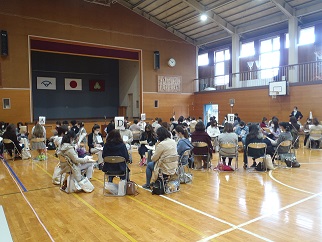 体育館で、大勢の参加者が「A」や「D」などのアルファベットが記されたプラカードを囲むように小さなグループに分かれて協議を行っている様子の写真