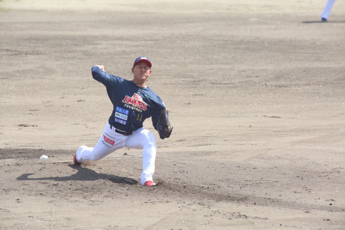 濃紺と赤のユニフォームを着た右投げのピッチャーが、大きく踏み込み、体をひねりながらボールをリ投げようとしている瞬間の写真