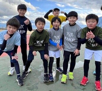 屋外運動場で、おそろいのTシャツを着た複数名の男の子がカメラに向かってポーズをとっている写真