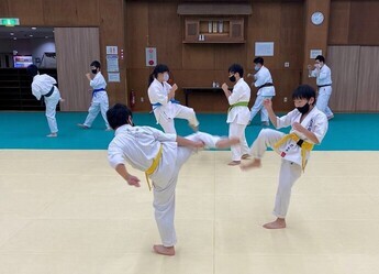 様々な色の帯を結んだ空手着姿の子どもたちが、マットが敷かれた練習場で2人一組で練習をしている様子の写真