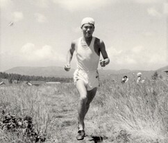 草の生い茂る開けた野原の道を背景の山々や晴れた空の下で力強く走り抜ける様子をとらえた円谷幸吉選手のモノクロ写真