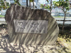 屋外に置かれた自然石の石碑に、「忍耐」という力強い文字と円谷幸吉選手の署名が刻まれたプレートがはめ込まれている、記念碑を正面から捉えた写真