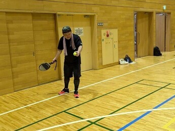 体育館で動きやすい服装をした男性が、左手にテニスボールを持ち、右手に持ったラケットを構えている写真