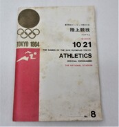 白い表紙に黒で「陸上競技」などの文字、金色で東京オリンピックのロゴマークプログラムが書かれ、左端には赤い長方形の背景に走っている人のピクトグラムが描かれた、全体的に古く汚れたプログラムの冊子の写真
