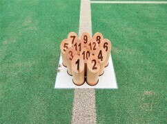 緑色の人工芝が敷かれた屋内競技場にて、1から12までの数字が天面に印字された木製のピン「スキットル」が、白いライン上の定位置に三角形の形状で隙間なくきれいに並べられている、モルック競技の接写写真