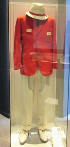 ガラスの展示ケースの中に、白地に赤のリボンが付いた帽子、赤いジャケット、白いスラックス、白い靴の、日本選手団の公式制服が立位の状態で展示されている写真