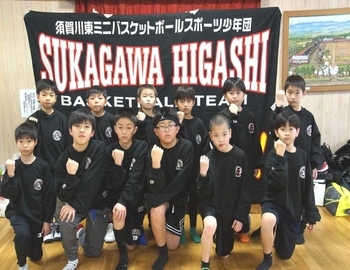 黒い背景に「SUKAGAWA HIGASHI」と大きく書かれた横断幕を背景に、黒い練習着を着た男子生徒たちが前後2列に並び、拳を見せて写した集合写真