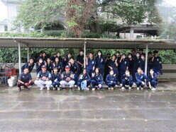 屋外の屋根の下に集合したジャージ姿のたくさんの生徒たちとレッドホープスの選手たちが並んで写した記念写真