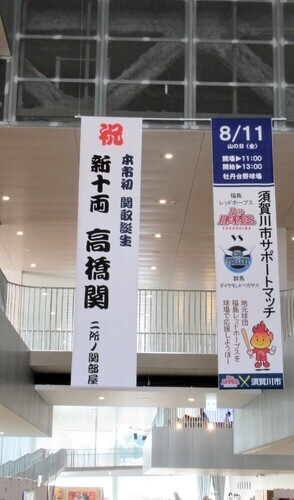 高い天井から、「祝新十両高橋関」と記された昇進を祝う大きな白い垂れ幕と、その隣に「須賀川市サポートマッチ」の開催を告知するポスター風の垂れ幕が並んで吊るされている、交流センター「tette」内のロビーの広々とした吹き抜け空間の写真