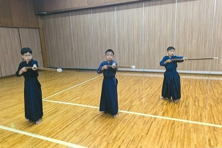 紺色の道着を着た3人の男の子が、横に並んで竹刀を正面に構えている写真