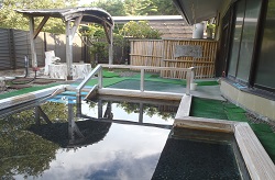 手前には木枠で縁取られた四角い浴槽がある竹垣の塀に囲まれた落ち着いた雰囲気の屋外露天風呂の写真