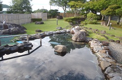 竹垣や木々に囲まれた手入れの行き届いた芝生の庭園に、岩で縁取られた風情ある露天風呂の写真