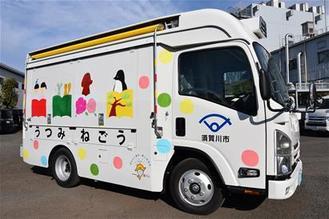 側面に色鮮やかな水玉模様と本などのイラストが描かれた白い移動図書館車が停車している写真