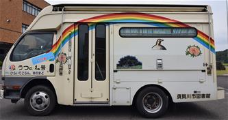側面に大きな虹と動物のイラストが描かれた移動図書館車が停車している写真
