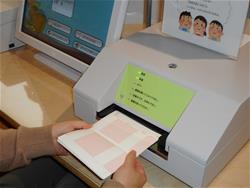 カウンターに設置された記帳用の機器に、手で持って開いた状態の読書の記録帳を挿入しようとしている様子写真