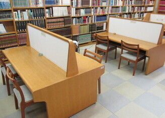 図書館内に木製の仕切り付き閲覧机と椅子がゆったり配置され、周囲を高い書架が囲む落ち着いた空間を写した写真