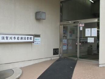 建物入口に須賀川市岩瀬図書館の看板が掲げられ、自動扉周辺に各種案内掲示が並ぶ様子の写真