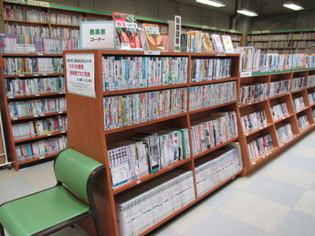 「農業書コーナー」と書かれた札のある茶色の書棚に、農業や園芸に関する書籍が多数陳列され、手前には緑色の椅子が一脚置かれている様子の写真