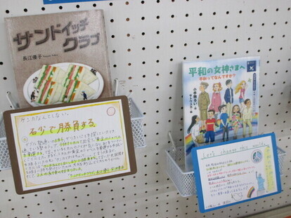 白い有孔ボードに設置されたラックに、「サンドイッチクラブ」と「平和の女神さまへ」という2冊の図書が手書きの紹介ポップと共に並べられている写真