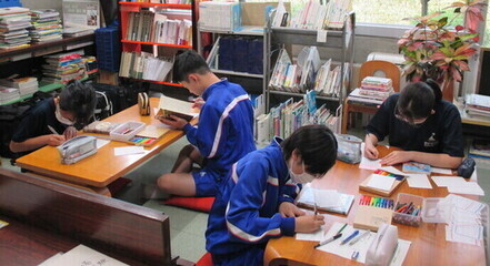 たくさんの本や書類が置かれた部屋で、2つのテーブルに2名ずつ分かれた生徒たちが、ポップを作っている写真