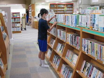 背の低い本棚の本に手を伸ばしている女子生徒の写真