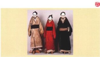 白い顔に独特の化粧を施した三体の人形が、左からベージュ、赤、黒の着物をそれぞれ着て立っている様子を正面から捉えた写真