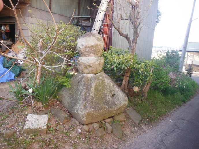 民家の脇に置かれた、苔むした台形の大きな石の上に丸みを帯びた二つの石が積み上げられた古舘五輪塔の写真