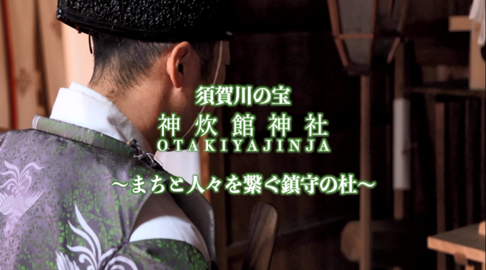 「須賀川の宝 神炊館神社 OTAKIYAJINJA 〜まちと人々を繋ぐ鎮守の杜〜」という緑色の縁取りテキストが、紫色の装束を身に纏い儀式に臨む神職の背中を近くから捉えた厳かな雰囲気の場面に重なっている写真