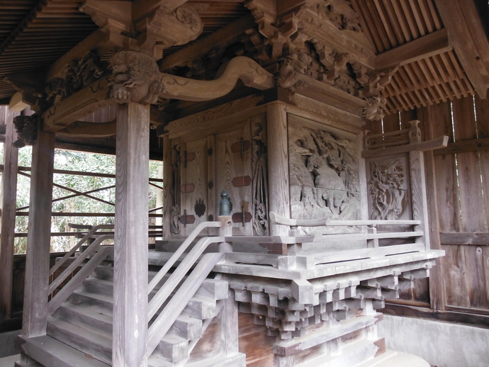 重厚な木造建築の神社本殿において、向拝の柱や梁には精巧な彫刻が施され、側面の脇障子や壁面にも緻密な浮き彫りが彫り込まれた熊野神社本殿の写真