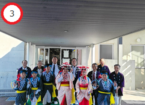 建物の軒下で、鮮やかな伝統衣装や法被を身にまとった子供たちと大人たちが前後に並んだ集合写真