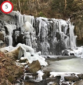 岩肌を流れる滝が寒さで白く凍りつき、周囲の岩や地面も雪と氷に覆われた、神秘的で力強い滝の風景を捉えた写真