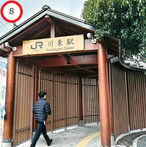 木材の太い柱と格子状の壁面が特徴的な和風のデザインで、入り口の上部に「JR川東駅」という駅名看板が掲げられたJR川東駅の駅舎と入口へ向かう男性の後ろ姿の写真