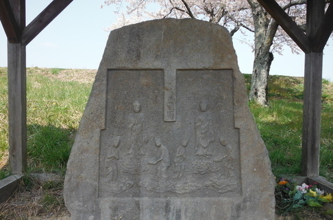 大きな石の表面の二つの区画に、雲に乗って降臨する阿弥陀如来や脇侍が繊細な浮き彫りで刻まれている石造双式阿弥陀三尊来迎供養塔の写真