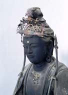 頭部を正面から捉えた、髪飾りをつけ伏し目がちに静かに佇む暗い色合いの菩薩像の上半身のアップ写真