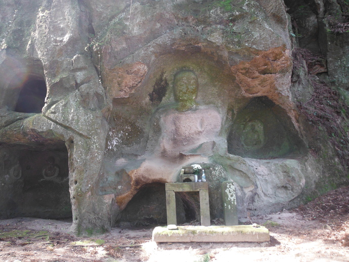 岩壁を大きく彫って形成された坐像の石仏が中央に刻まれ、手前に花などが供えられている和田大仏の写真