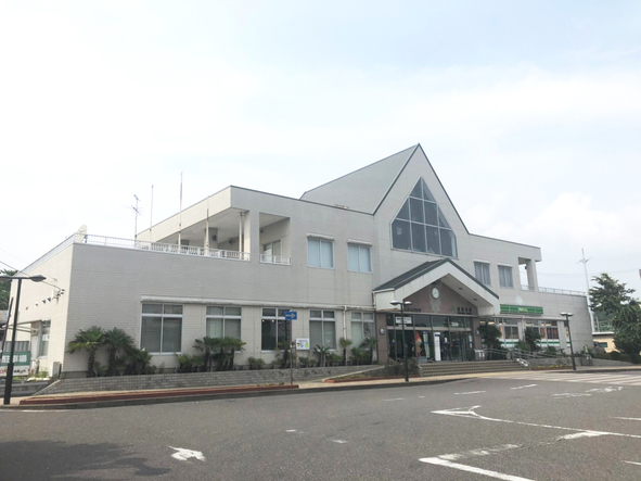 道路に面して建つ、中央の三角屋根が特徴的な、白い外壁のコミュニティプラザの外観写真