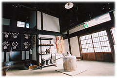 紺色の暖簾がかかった通路と入口のドアがある土間の中央に杵臼が置かれている写真