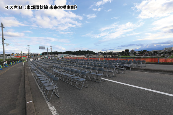 広く澄み渡る青空の下、東部環状線の路上に数多くの黒い折り畳み椅子が整然と並べられ、観覧席が設営されたイスB席（東部環状線 未来大橋南側）の写真