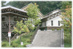 木々に囲まれ、幅の広い長い階段の上に白い壁の洋風の建物が建っている、公園管理センターの外観写真