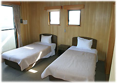 木目の壁で大きな窓がある部屋に2つのベッドが間をあけて並んでいる寝室の写真