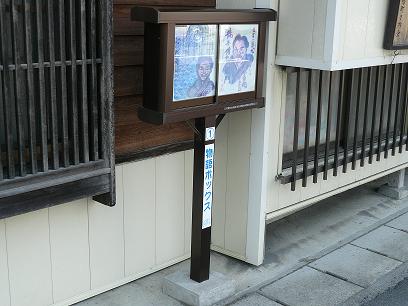 白い壁で窓に格子が付いた建物の外に設置された、偉人のイラストや説明が書きこまれた物語ボックスの写真