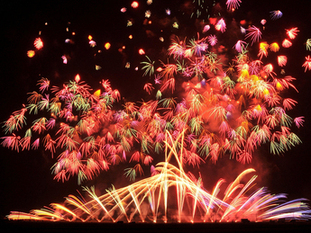 地上付近から扇状に黄金色の花火の光が広がり、その上空では赤や緑、オレンジ色火花が幾重にも重なり合いながら夜空を彩る花火大会の様子の写真