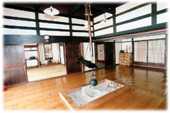 広々とした板の間の中央に、鉄瓶が吊るされた囲炉裏がある居間の写真