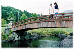 緑豊かな景色を背景に、桟橋の上に2人の女性が立ち、下を流れる水を眺めている様子の写真