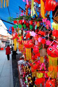 色鮮やかな飾り物が屋台にびっしりと吊り下がり、通りを歩く人々のそばで鮮烈な賑わいを放つ写真