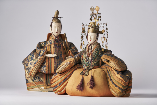 豪華な衣装を着た二体の享保雛人形が並び、手前は金色の衣装に緑や紫の装飾を施し頭に華やかな冠を付け、奥は青と金を基調とした衣装をまとい手に巻物を持つ姿で、全体に精緻な刺繍と立体的な袖が特徴的な写真