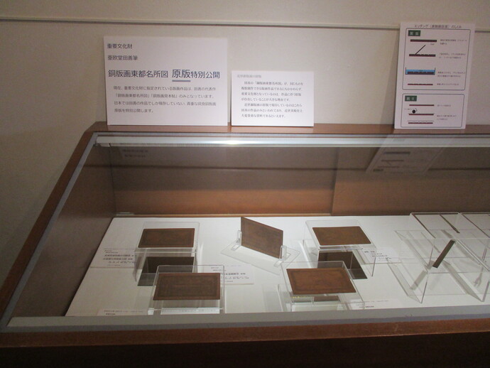 アクリルケースに入った四角い銅版画の原版が複数並べて展示ケースの中に展示され、上に説明文が添えられている写真